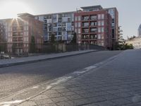 the sidewalk by the street is empty and sun shines on it and the city has very tall buildings in front