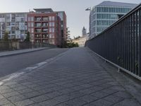 the sidewalk by the street is empty and sun shines on it and the city has very tall buildings in front