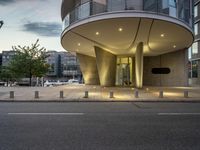 the curved structure in front of a large building in a city at night time, illuminated by lamps