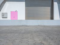 a bright pink door stands outside a white wall and brick floor of an open garage