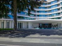 a building with many floors and windows with grass in front of it and the sign welcomes all on