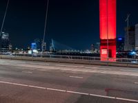 an overpass bridge with cars moving at night in the city with skyscrapers lit up in red