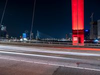 an overpass bridge with cars moving at night in the city with skyscrapers lit up in red