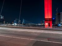 an overpass bridge with cars moving at night in the city with skyscrapers lit up in red