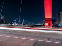 an overpass bridge with cars moving at night in the city with skyscrapers lit up in red