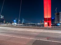 an overpass bridge with cars moving at night in the city with skyscrapers lit up in red