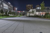 the sidewalk and the grass are illuminated by light fixtures at night, next to an office building