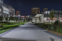 the sidewalk and the grass are illuminated by light fixtures at night, next to an office building