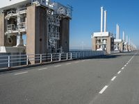 a bridge over the ocean with construction equipment in the background and two people walking on it