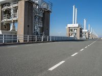 a bridge over the ocean with construction equipment in the background and two people walking on it