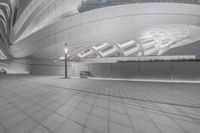 the man is walking towards an empty building that has curves on it and an open walkway with benches around