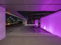 a concrete street with multiple floors and purple lighting on the side of the building, a sidewalk beside it