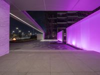 a concrete street with multiple floors and purple lighting on the side of the building, a sidewalk beside it