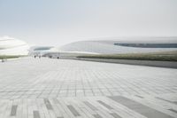 people walking on concrete pavement in front of large white buildings with geometric shapes and columns