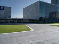 a large grey building sits in a parking lot near grassy area and a tree trunk