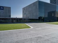 a large grey building sits in a parking lot near grassy area and a tree trunk