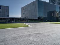 a large grey building sits in a parking lot near grassy area and a tree trunk