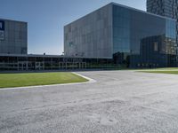 a large grey building sits in a parking lot near grassy area and a tree trunk