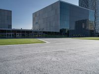 a large grey building sits in a parking lot near grassy area and a tree trunk