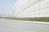 an empty path outside a building and some bushes and trees with the city in the background