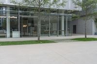 a glass walled building with many stores and trees in the sidewalk outside of it next to the grass