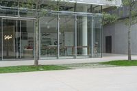 a glass walled building with many stores and trees in the sidewalk outside of it next to the grass