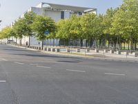 an empty street in front of a building and trees in the middle of the road