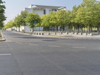 an empty street in front of a building and trees in the middle of the road