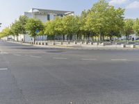 an empty street in front of a building and trees in the middle of the road