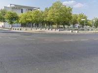 an empty street in front of a building and trees in the middle of the road