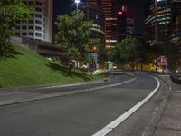 a city street at night with street signs and lights on it is empty the pavement in front of a grassy hillside