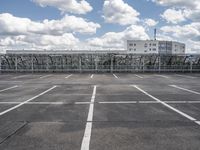 an empty parking lot with some buildings in the background and a blue sky with white clouds above it