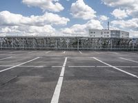 an empty parking lot with some buildings in the background and a blue sky with white clouds above it