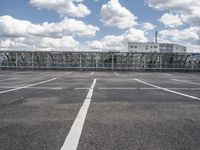 an empty parking lot with some buildings in the background and a blue sky with white clouds above it