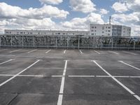 an empty parking lot with some buildings in the background and a blue sky with white clouds above it