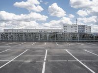 an empty parking lot with some buildings in the background and a blue sky with white clouds above it