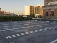 a empty parking lot with trees and buildings in the background as the sun sets in