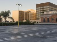 a empty parking lot with trees and buildings in the background as the sun sets in