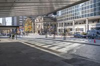 a view of buildings from the sidewalk in front of it, with a bus, cars, and orange cones