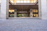 a sidewalk outside of a very large building with several windows and glass walls and large pillars