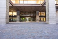 a sidewalk outside of a very large building with several windows and glass walls and large pillars
