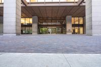 a sidewalk outside of a very large building with several windows and glass walls and large pillars