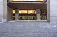 a sidewalk outside of a very large building with several windows and glass walls and large pillars