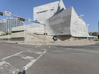 a city intersection and traffic lights on a clear day in the sun a city building with two sides covered in concrete