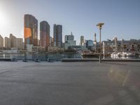 a man rides a skateboard down a paved sidewalk at sunset in the city skyline