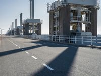 a bridge over the ocean with construction equipment in the background and two people walking on it