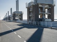 a bridge over the ocean with construction equipment in the background and two people walking on it