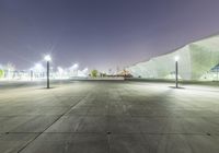 a empty concrete courtyard with a parking meter next to it at night time with lights in the sky