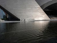 a photo of a big structure with water in it with people walking around it, and people walking about in front