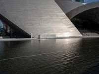 a photo of a big structure with water in it with people walking around it, and people walking about in front